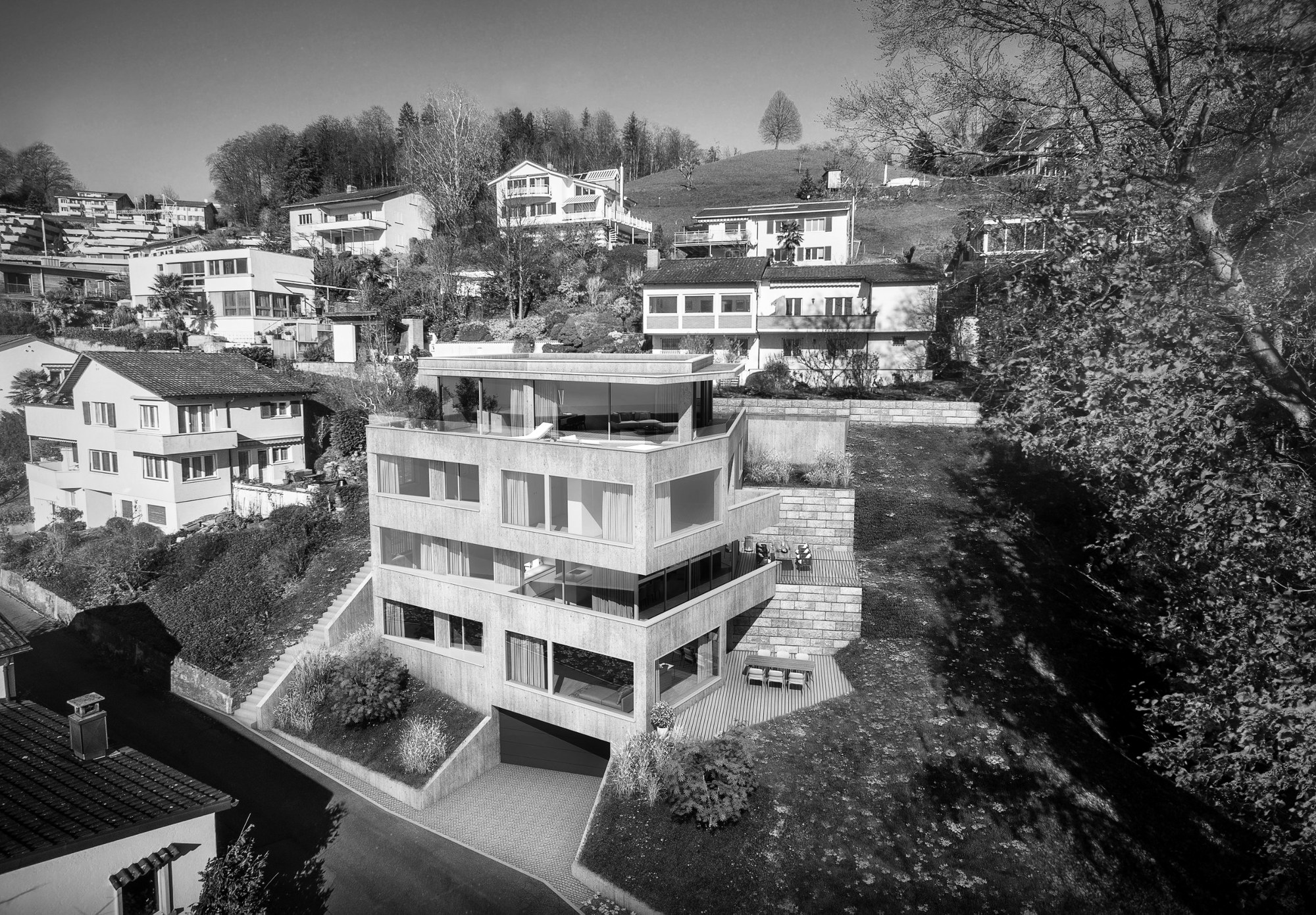 Luftbild des Mehrfamilienhauses am Hang mit Terrassen und Garageneinfahrt